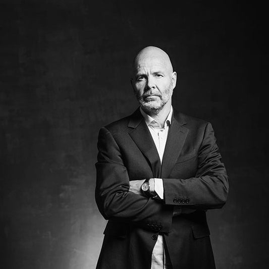 Mustavalkoinen muotokuva kirjailija Jukka Hakalasta. Hän seisoo vakavana katsoen suoraan kameraan, kädet ristissä rinnallaan. Hakala on pukeutunut tyylikkääseen pukuun, ja tausta on tumma ja tekstuuriltaan elävä.