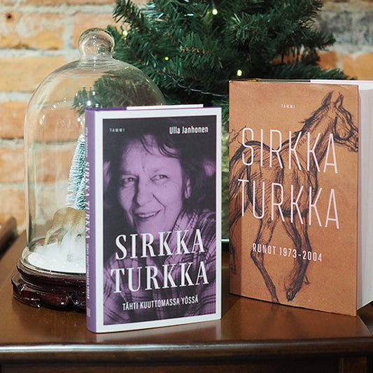 Puupöydällä tiiliseinän edustalla on kaksi kirjaa ja joulukoristeita. Vasemmalla Ulla Janhosen kirjoittama Sirkka Turkan elämäkerta 'Tähdet kuuttomassa yössä'. Oikealla Sirkka Turkan runokokoelma 'Runot 1973–2004'.