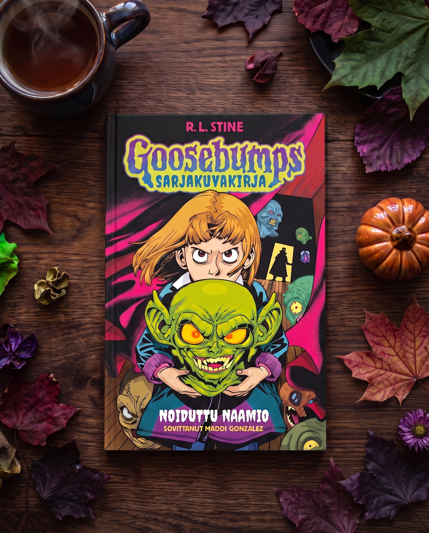 Kuvassa on R. L. Stinen Goosebumps-sarjakuvakirja: Noiduttu naamio puisella pöydällä. Kirjan ympärillä on syksyn lehtiä, kurpitsa ja teekuppi.