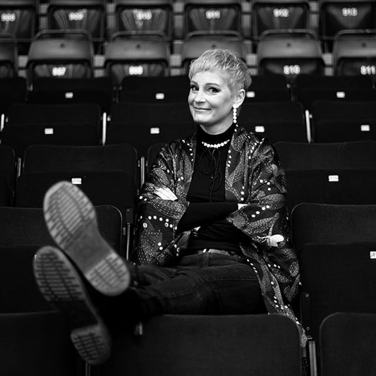 Mustavalkoinen kuva kirjailija Annukka Salamasta istumassa katsomossa. Salama katsoo kameraan ja hymyilee.