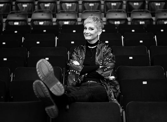 Mustavalkoinen kuva kirjailija Annukka Salamasta istumassa katsomossa. Salama katsoo kameraan ja hymyilee.