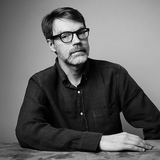 Mustavalkoisessa kuvassa Antti Ukkonen istuu pöydän ääressä ja katsoo kameraan. Hänellä on silmälasit ja tumma kauluspaita. Tausta on yksivärinen.
