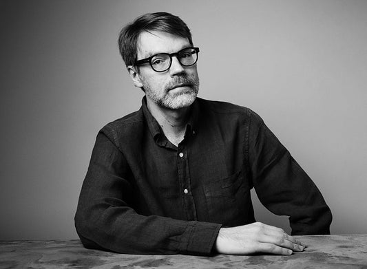 Mustavalkoisessa kuvassa Antti Ukkonen istuu pöydän ääressä ja katsoo kameraan. Hänellä on silmälasit ja tumma kauluspaita. Tausta on yksivärinen.