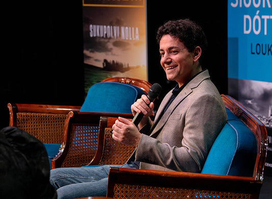 Chris Whitaker istuu lavalla tuolissa ja pitää kädessään mikrofonia. Taustalla näkyy kirjan julisteita ja lavan sininen sohva.