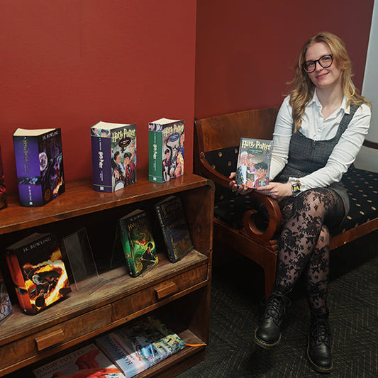 Maija Lang istuu sohvalla vierellään kirjahylly, jossa on lukuisia Harry Potter -kirjoja.