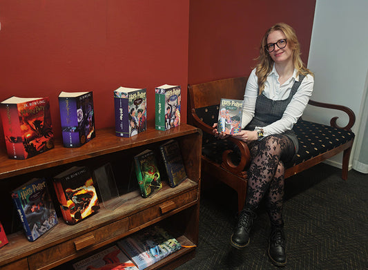 Maija Lang istuu sohvalla vierellään kirjahylly, jossa on lukuisia Harry Potter -kirjoja.