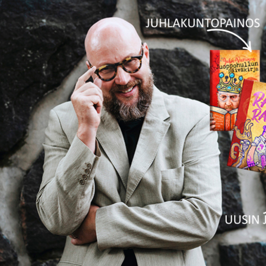 Kirjailija Juha Vuorinen hymyilee kiviseinän edessä. Vieressä näkyvät Juoppohullun päiväkirja -sarjan juhlapainos ja uusin osa Raivoraitis.