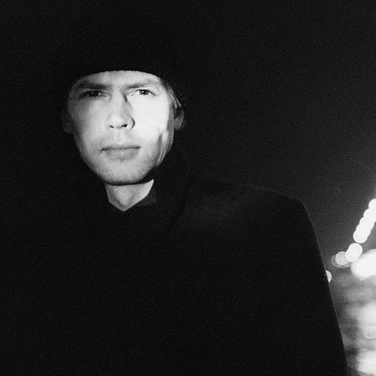 Mustavalkoinen puolikuva kirjailija Ilkka Remeksestä. Remeksen taustalla näkyy epätarkkana kaupungin valoja.