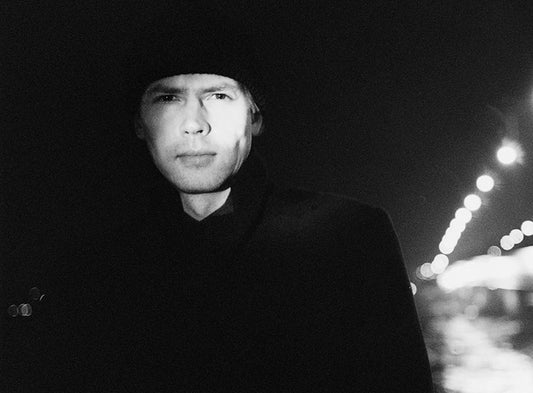 Mustavalkoinen puolikuva kirjailija Ilkka Remeksestä. Remeksen taustalla näkyy epätarkkana kaupungin valoja.