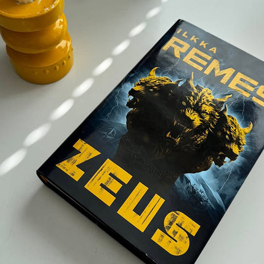 Ilkka Remeksen Zeus-kirja pöydällä keltaisen kynttilänjalan vieressä, kirja heijastuupeilistä 