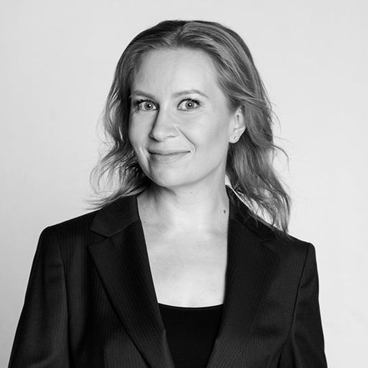 Mustavalkoinen muotokuva kirjailija Vera Valasta. Hän seisoo puolikuvassa, pukeutuneena mustaan jakkuun ja toppiin, katse suunnattuna hieman kameran ohi ja hymyillen kevyesti. Hänen vaaleat hiuksensa laskeutuvat olkapäille, ja taustalla on vaaleaa.