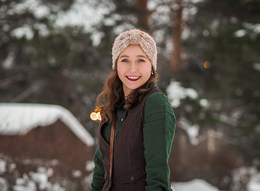 Kirjailija Lotta-Sofia Saahko hymyilee talvisessa ulkomaisemassa. Hänellä on päässään vaalea neulepanta, vihreä pusero ja ruskea liivi. Taustalla näkyy lumisia puita ja hämärtyvän illan valoja.