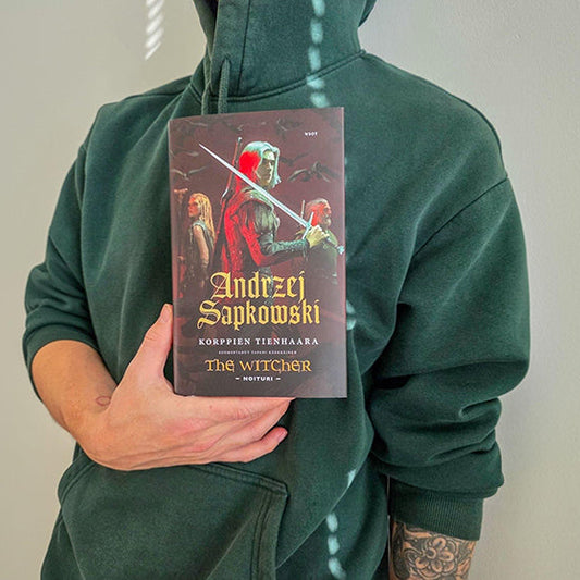 Huppariin pukeutunut henkilö pitää käsissään Andrzej Sapkowskin kirjaa ”Korppien tienhaara”. Kirjan kannessa on tumma fantasiakuva, jossa näkyy useita hahmoja ja miekka.