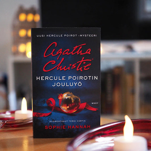 Kuvassa Hercule Poirotin jouluaiheinen romaani seisoo pöydällä litteän kynttilän ja punaisten lasiesineiden keskellä. Taustalla näkyy hämärästi valaistu olohuone ja jouluvaloja.