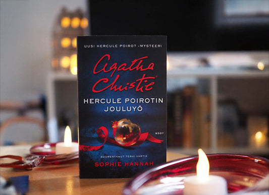 Kuvassa Hercule Poirotin jouluaiheinen romaani seisoo pöydällä litteän kynttilän ja punaisten lasiesineiden keskellä. Taustalla näkyy hämärästi valaistu olohuone ja jouluvaloja.