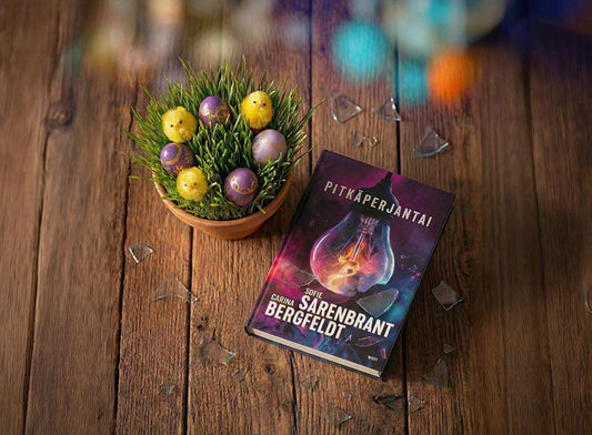 Puisella pöydällä on kirja Pitkäperjantai, tekijä Sofie Sarenbrant. Kirjan vieressä on kulho, jossa on ruohoa, värjättyjä pääsiäismunia ja pieniä keltaisia tipuja. Pöydällä on myös lasinsirpaleita.