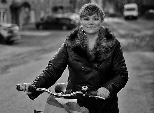 Mustavalkoisessa kuvassa Essi Kummu seisoo kadulla polkupyörän takana ja pitää kiinni ohjaustangosta. Hän katsoo kameraan ja on pukeutunut tummaan takkiin, jossa on leveä karvakaulus. Pyörän etukorissa on paperikassi. Taustalla epätarkkoja rakennuksia.