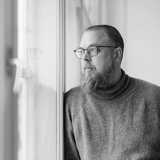 Mustavalkoinen puolikuva kirjailija Tuomas Kyröstä nojaamassa ikkunaan ja katsomassa siitä ulos.