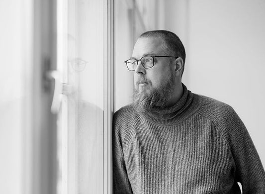 Mustavalkoinen puolikuva kirjailija Tuomas Kyröstä nojaamassa ikkunaan ja katsomassa siitä ulos.
