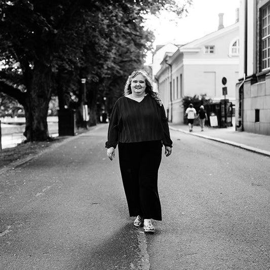 Mustavalkoinen valokuva kirjailija Thua Aallosta kävelemässä kadulla puiden ja rakennusten reunustamassa kaupunkimaisemassa.