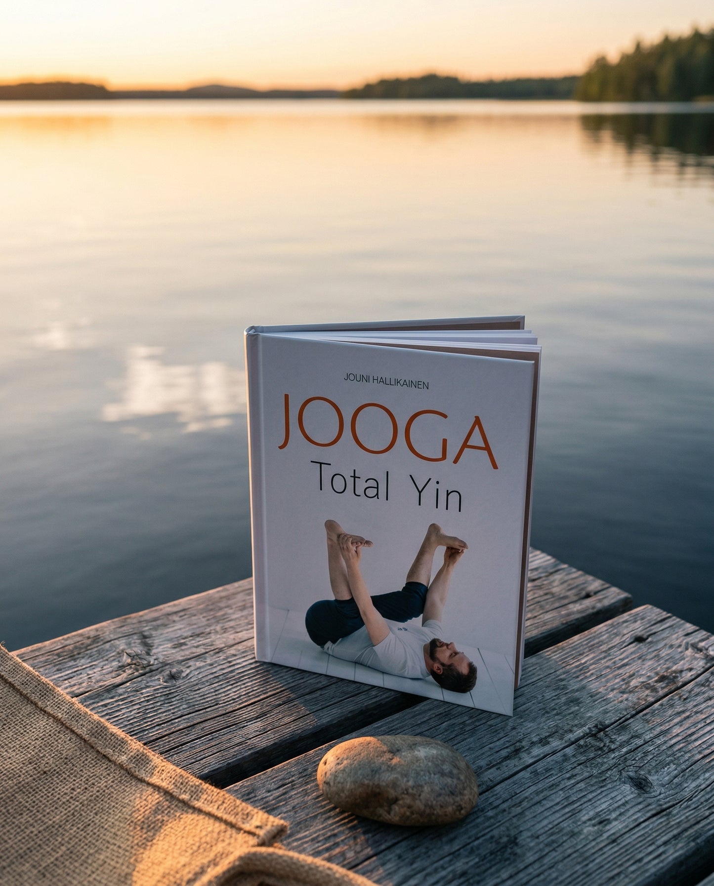 Laiturilla järven rannalla on kirja Jooga Total Yin, tekijä Jouni Hallikainen. Kirjan vieressä on kivi ja kangaspala, ja taustalla näkyy tyyni järvimaisema auringonlaskun valossa.